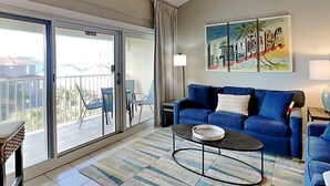 Una sala de estar con un sofá azul, una mesa de centro y un balcón con sillas.