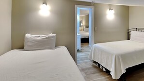 Un dormitorio con dos camas, piso de madera y una puerta que da a otra habitación.