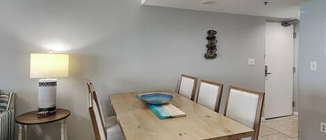 A dining area with a wooden table and cushioned chairs, a side table with a lamp, and a decorative wall piece.