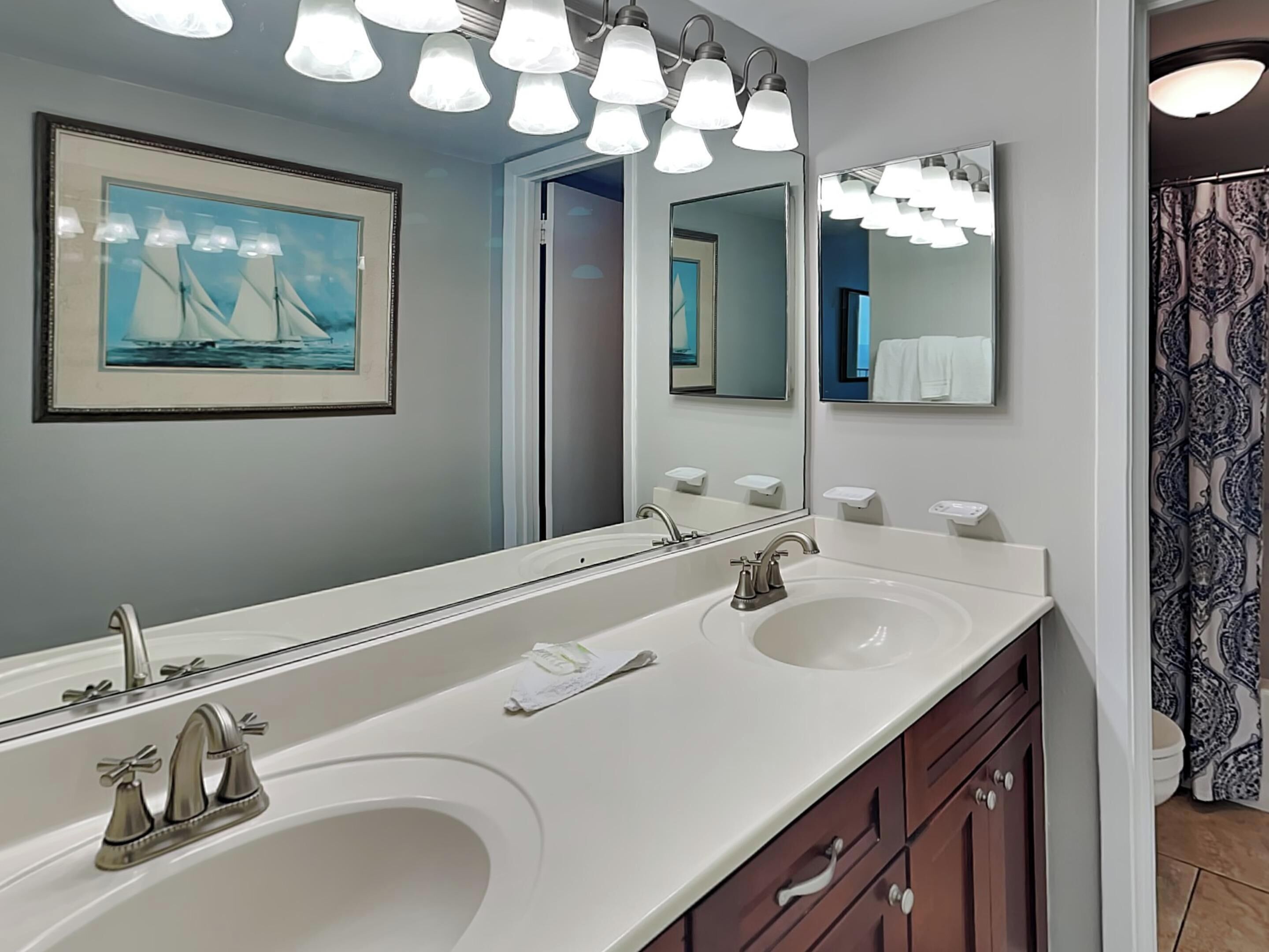 Une salle de bain avec deux lavabos, un grand miroir et un éclairage au plafond.