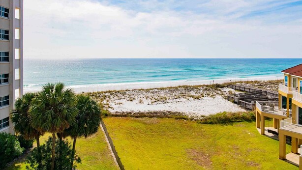 A beachfront view with a building, a grassy area, and a sandy beach. - Regency Towers #508 West | Gulf Views, Pool! (Pensacola Beach)