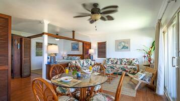 A dining area with a round glass table, wooden chairs, and a ceiling fan.