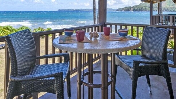 Mesa redonda com duas cadeiras de vime numa varanda com vista para o mar.