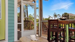 A porch with a wooden table and chairs, a door, and a view of trees and a mountain. - Designer Home, New Gulf View Home with Comm. Pool ~ Bethany Cottage (Indian Pass)