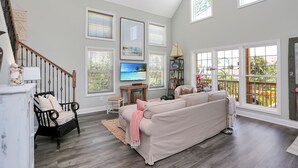 A spacious living room with a large beige sofa, a black chair, and a television on a wooden stand. - Designer Home, New Gulf View Home with Comm. Pool ~ Bethany Cottage (Indian Pass)