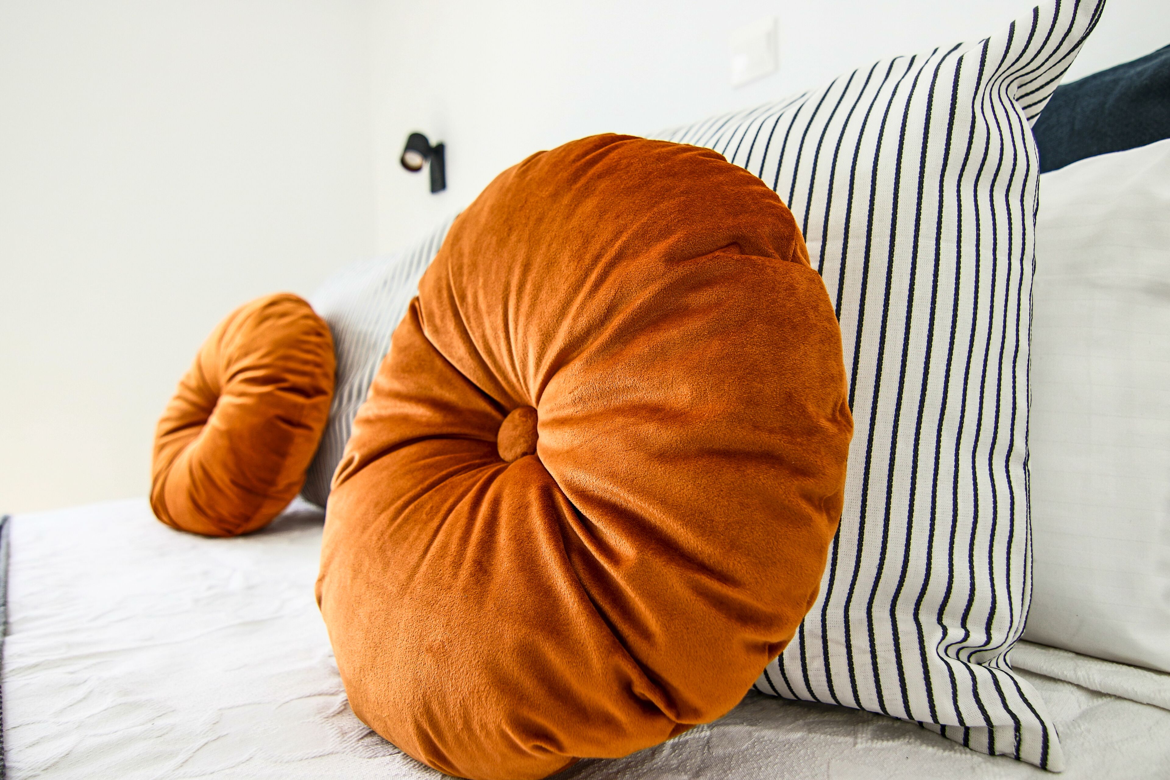 Una cama con almohadones a rayas y un cojín redondo color naranja.
