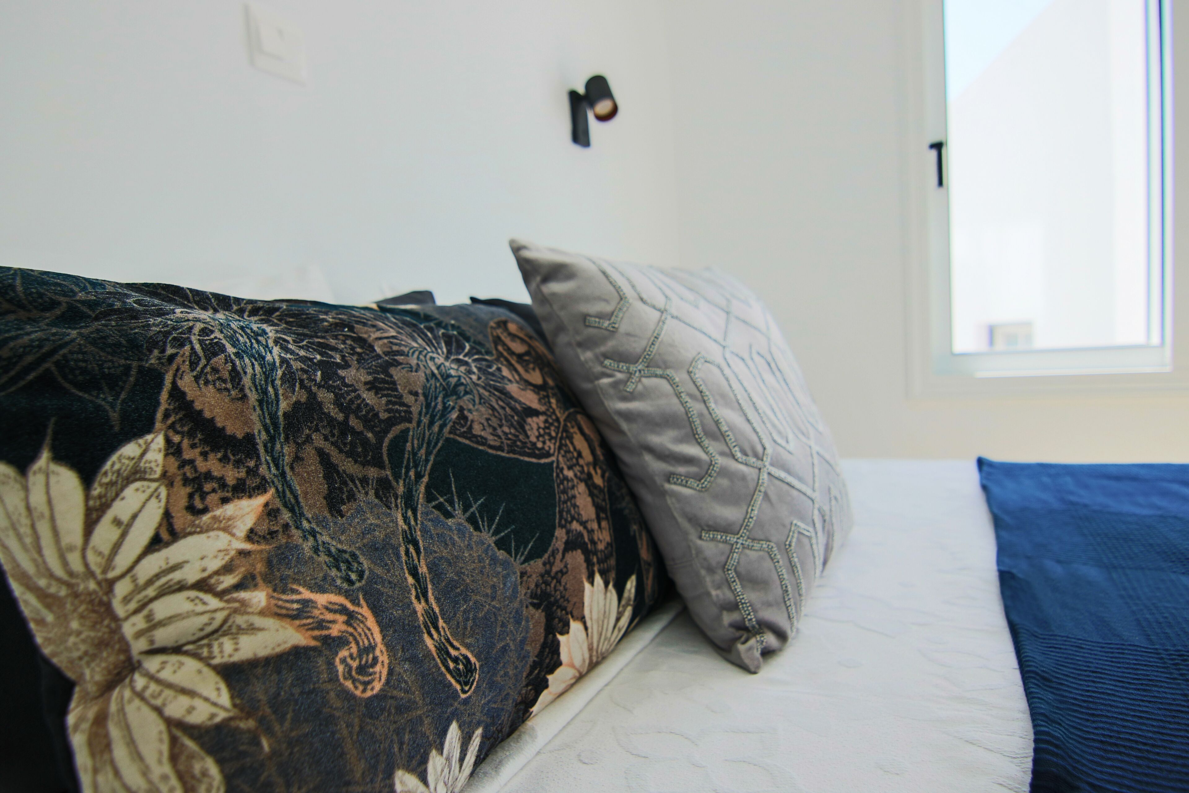 Ein Bett mit einer floralen Decke, einem grauen Kopfkissen und einer blauen Decke.