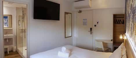 Habitación de hotel con cama, escritorio, silla, televisor, ducha y armario.