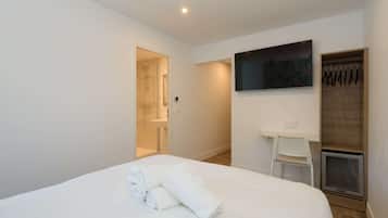 Une chambre d’hôtel avec un lit, un téléviseur fixé au mur, un petit bureau et un espace douche visible à travers une porte ouverte.