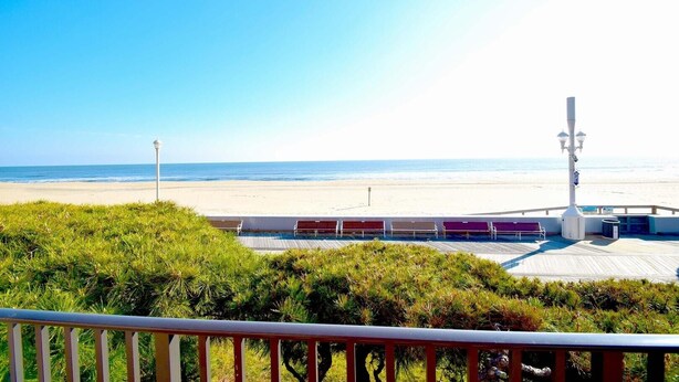 Blick auf einen Strand vom Balkon mit Geländer, einer Holzterrasse und einem weißen Laternenpfahl.