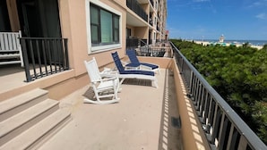 Ein Balkon mit zwei weißen Schaukelstühlen und einem Tisch mit Blick auf Strand und Meer.
