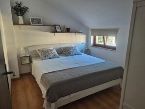 A bedroom with a bed, bedside tables, a window, and a shelf with decorative items.