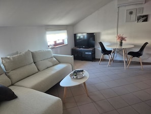 A living room with a sofa, a TV, a small table, and two chairs.