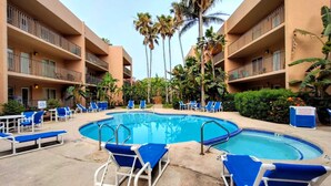 Un espace piscine d’hôtel avec des chaises longues bleues, une piscine centrale et des palmiers.