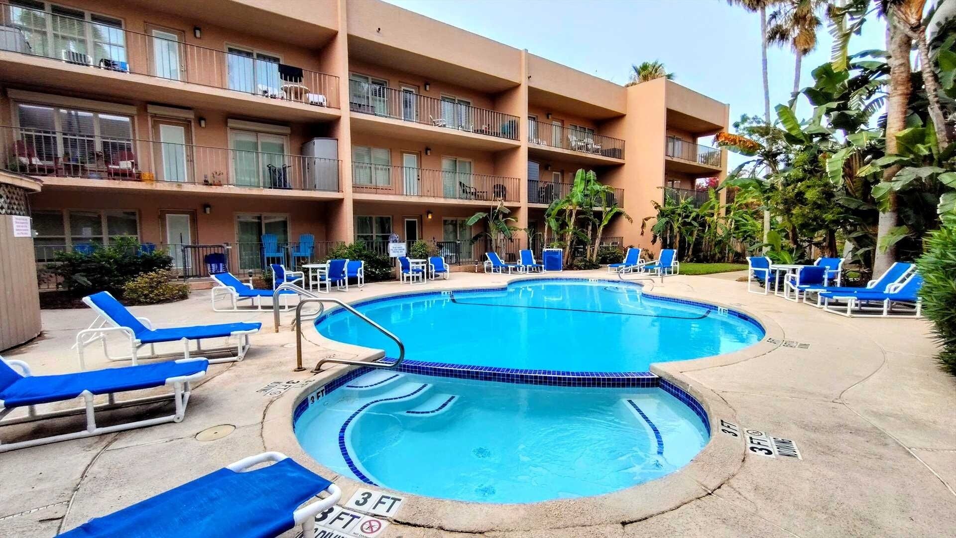 A hotel with a pool area, blue lounge chairs, and a multi-story building with balconies.