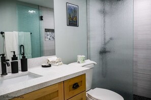 A bathroom with a white sink, black faucets, a mirror, a toilet, and a glass shower enclosure.