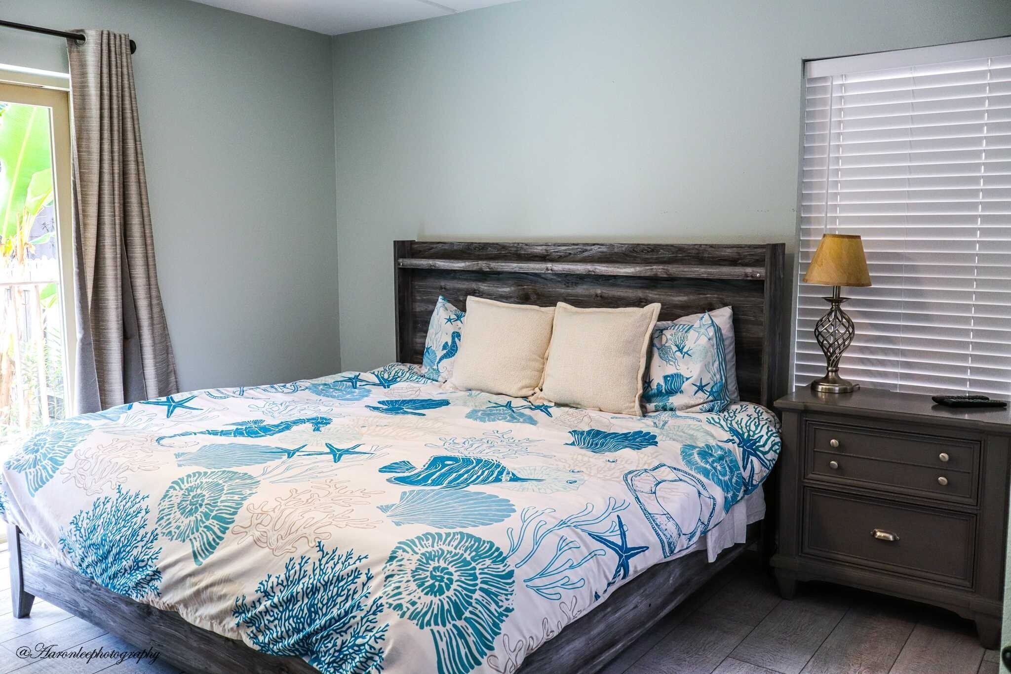 A bedroom with a bed, nightstand, and window with blinds.