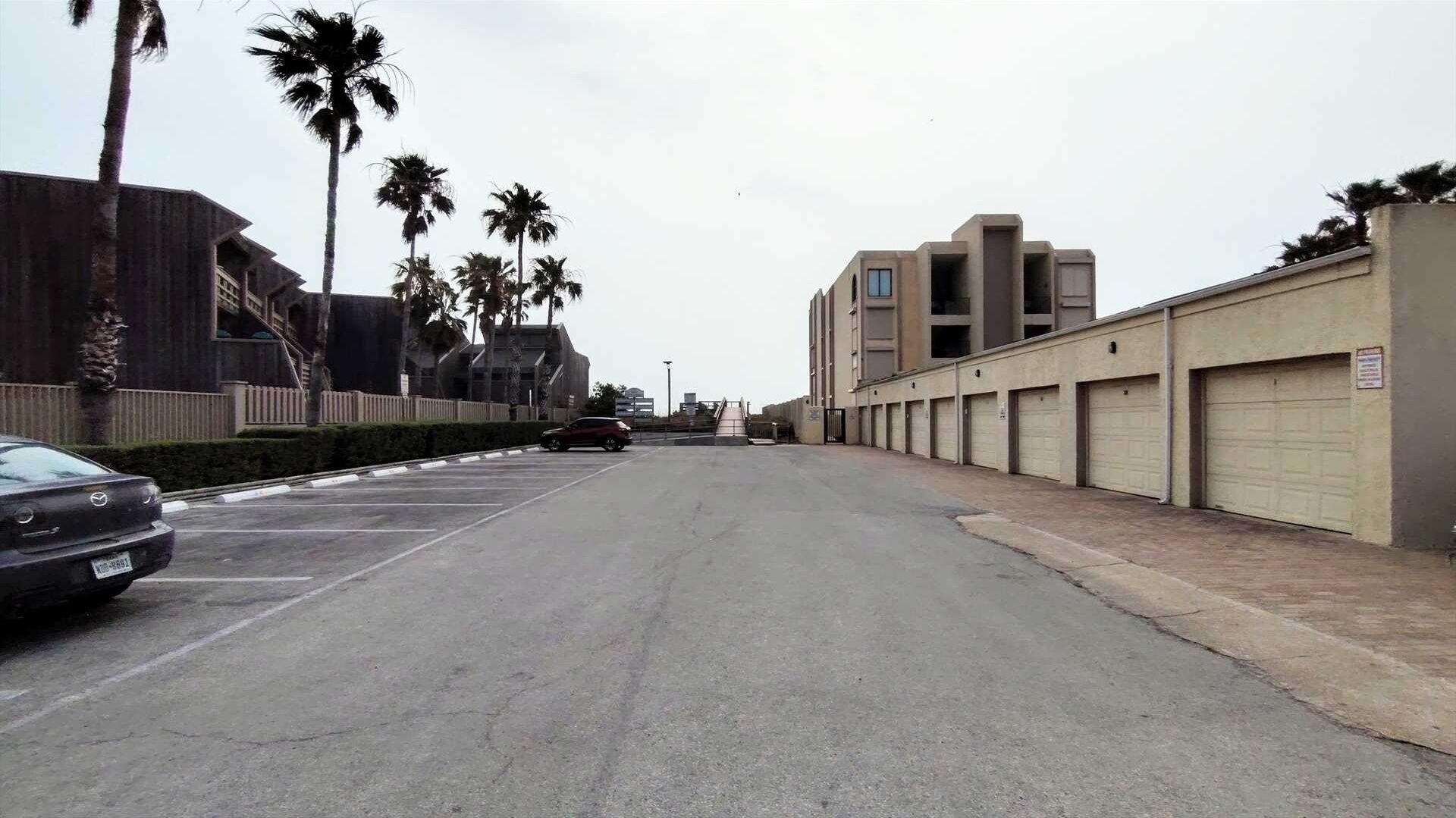 A parking lot with a car, a building with multiple garage doors, and palm trees.