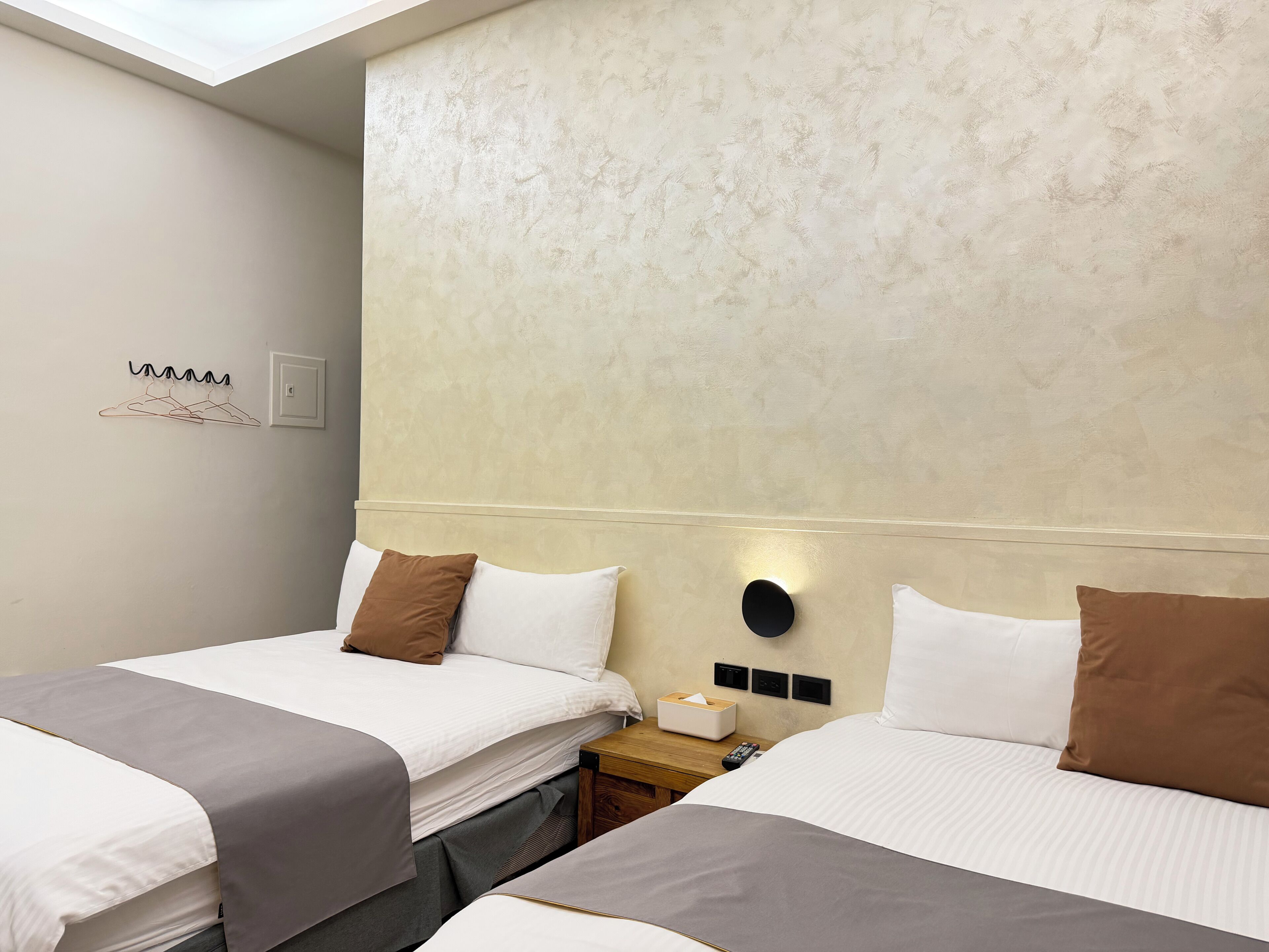 Habitación de hotel con dos camas, una mesita de noche, una lámpara de pared y una lámpara en el techo.
