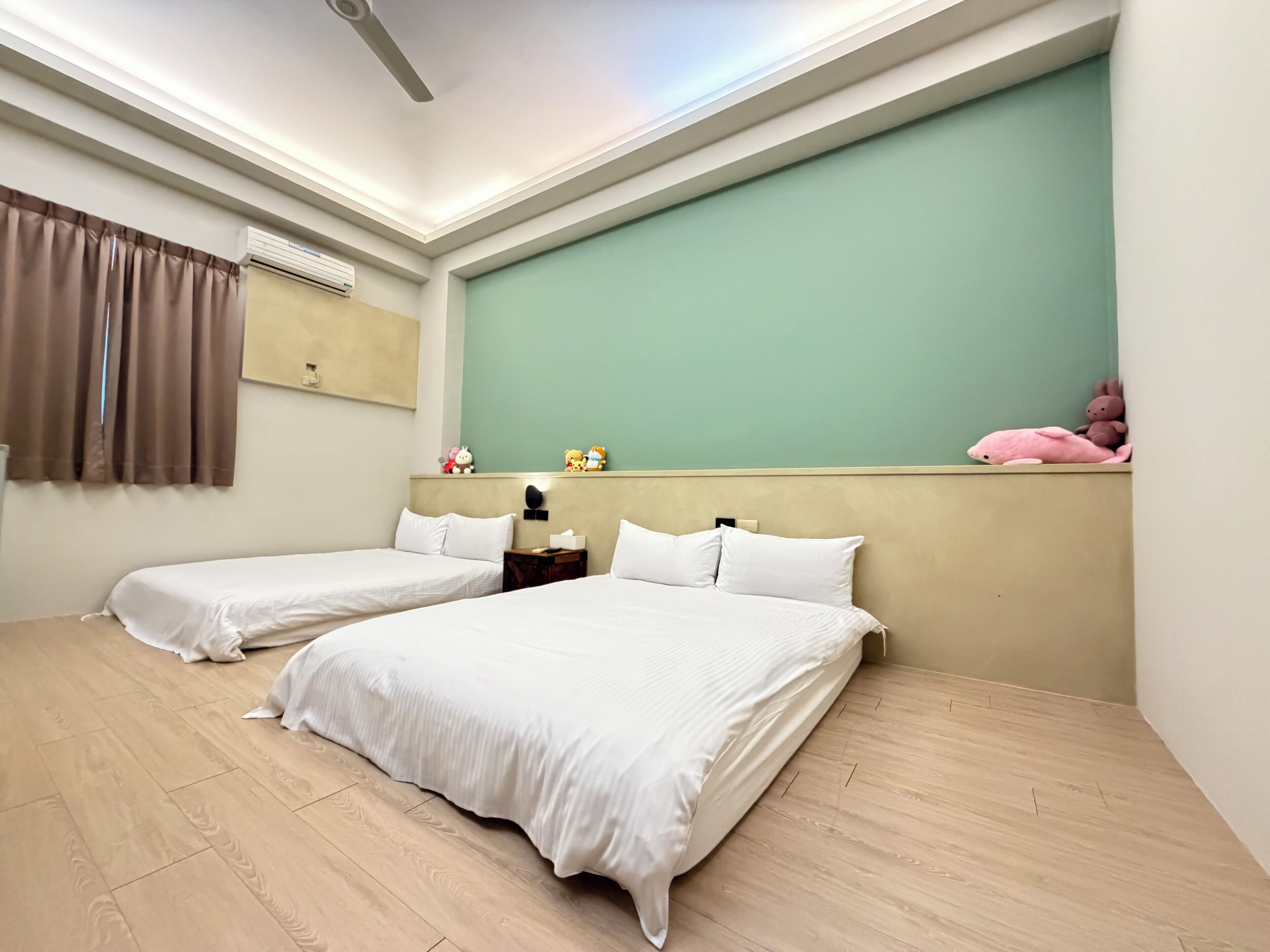 A hotel room with two beds, a ceiling fan, a wall-mounted air conditioner, and a green accent wall.
