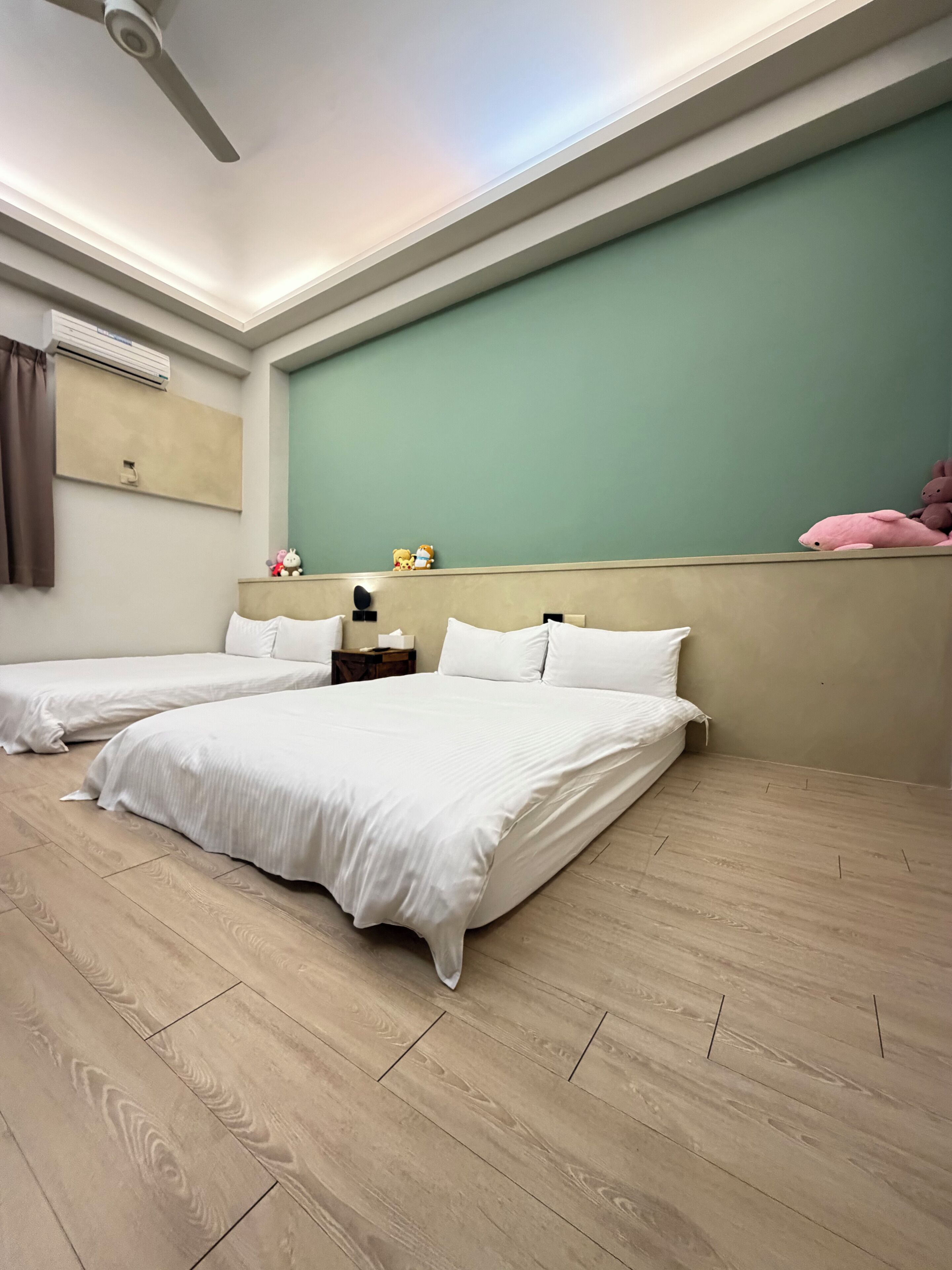 A hotel room with two beds, a ceiling fan, an air conditioning unit, a nightstand, and a green wall.