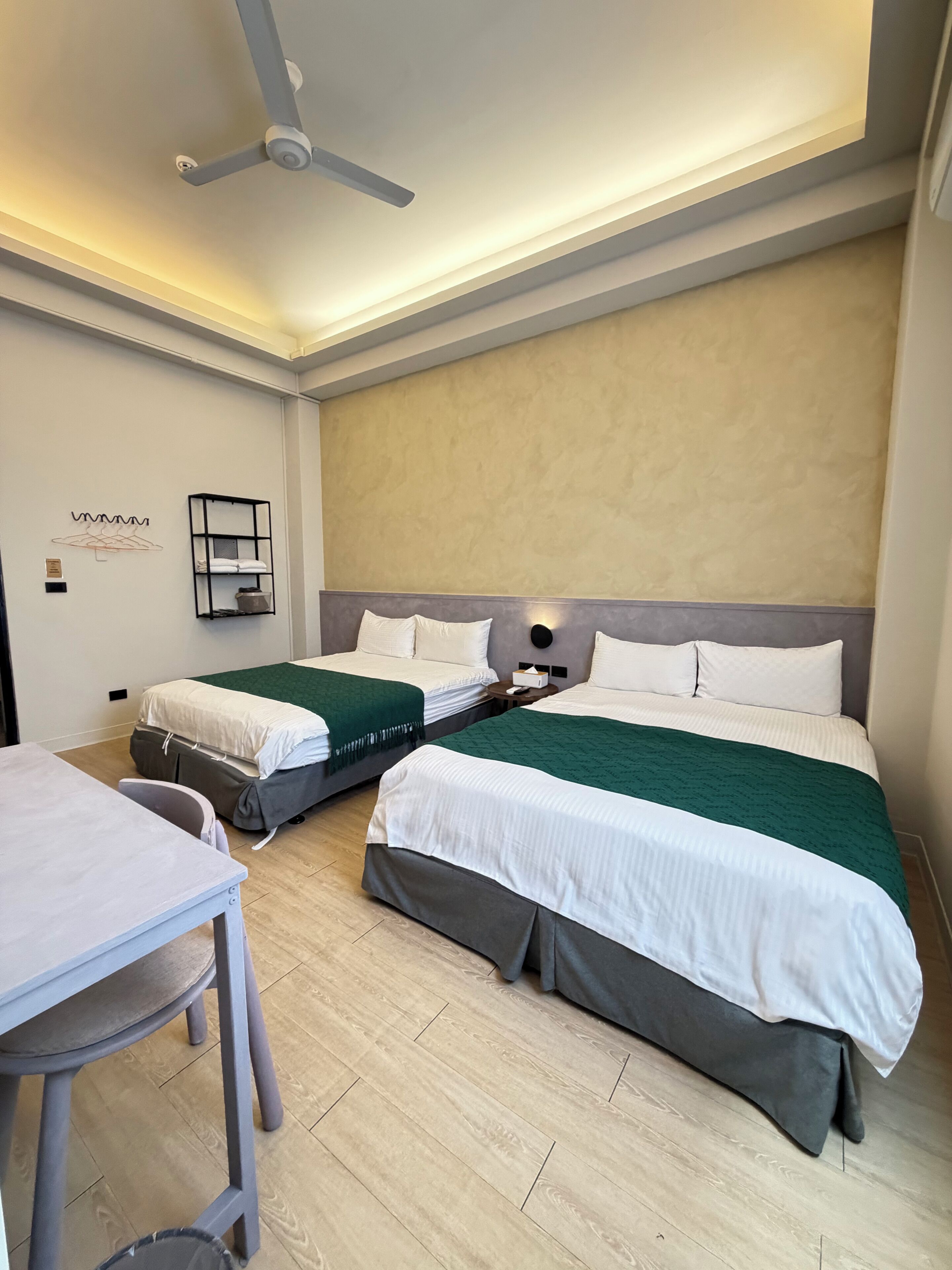 Une chambre d’hôtel avec deux lits, un bureau et un ventilateur de plafond.