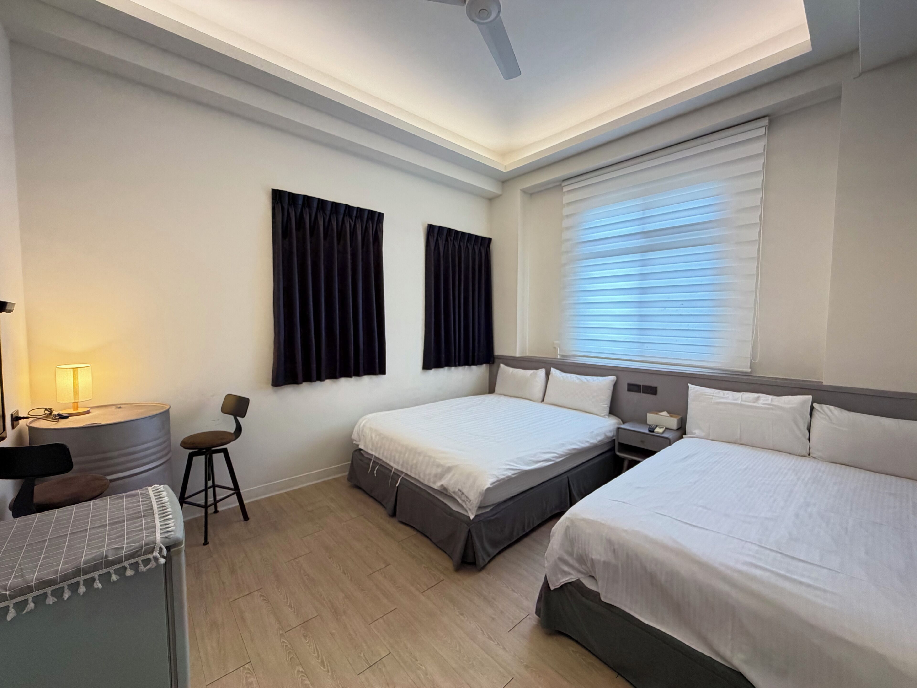 A hotel room with two beds, a desk, a chair, a lamp, and a ceiling fan.