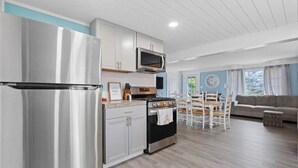 Una cucina moderna con elettrodomestici in acciaio inossidabile, un'area pranzo con tavolo e sedie in legno e un soggiorno con divano e finestra.