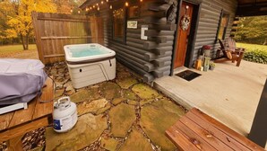 Un rustico chalet con vasca idromassaggio, patio in pietra e terrazza in legno.