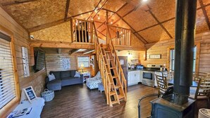 Accogliente interno di una baita con camera soppalcata, camino, pavimenti in legno e angolo cottura.