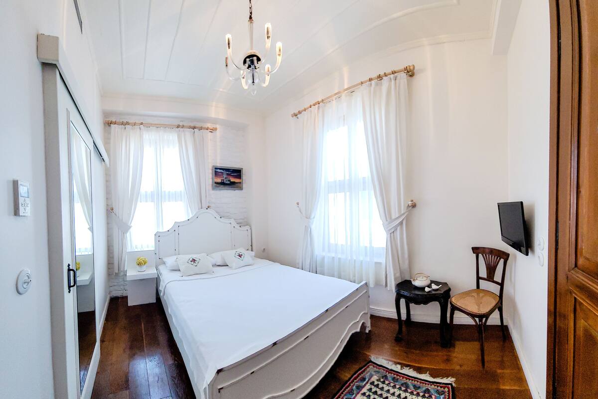 A bedroom with a bed, a chair, a television, and a window with curtains.