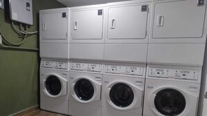 Sala de bugaderia amb diverses rentadores i assecadores, un panell de control i una caixa elèctrica penjada a la paret.