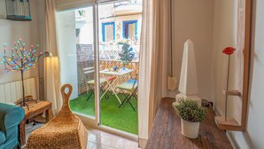 A room with a sliding glass door leading to an outdoor area with a table and chairs, a wicker chair, a potted plant, and a wall-mounted light fixture. - The Beach Holi Apartment by Hello Homes Sitges (Sitges)
