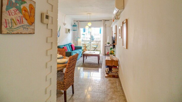 A narrow hallway leading to a living room with a sofa, a dining table with chairs, and a small side table. - The Beach Holi Apartment by Hello Homes Sitges (Sitges)
