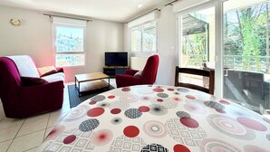Un salon avec un téléviseur, des fauteuils rouges, une table et de grandes fenêtres donnant sur la forêt.