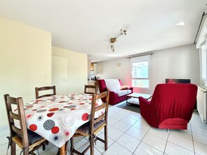 A dining area with a table and chairs, a sofa, a television, and a window with a view of buildings. - Comfortable T3 at the foot of the Castle of Chambéry! (Chambéry)