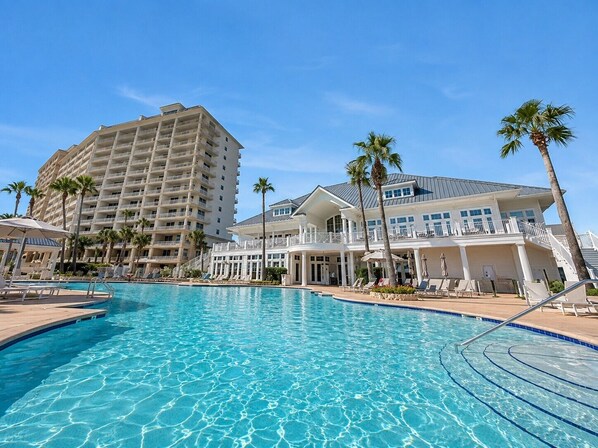 A swimming pool with clear blue water, surrounded by palm trees and a large hotel building in the background.