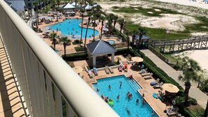 Een resort met meerdere zwembaden, een strand en een hoog gebouw op de achtergrond.