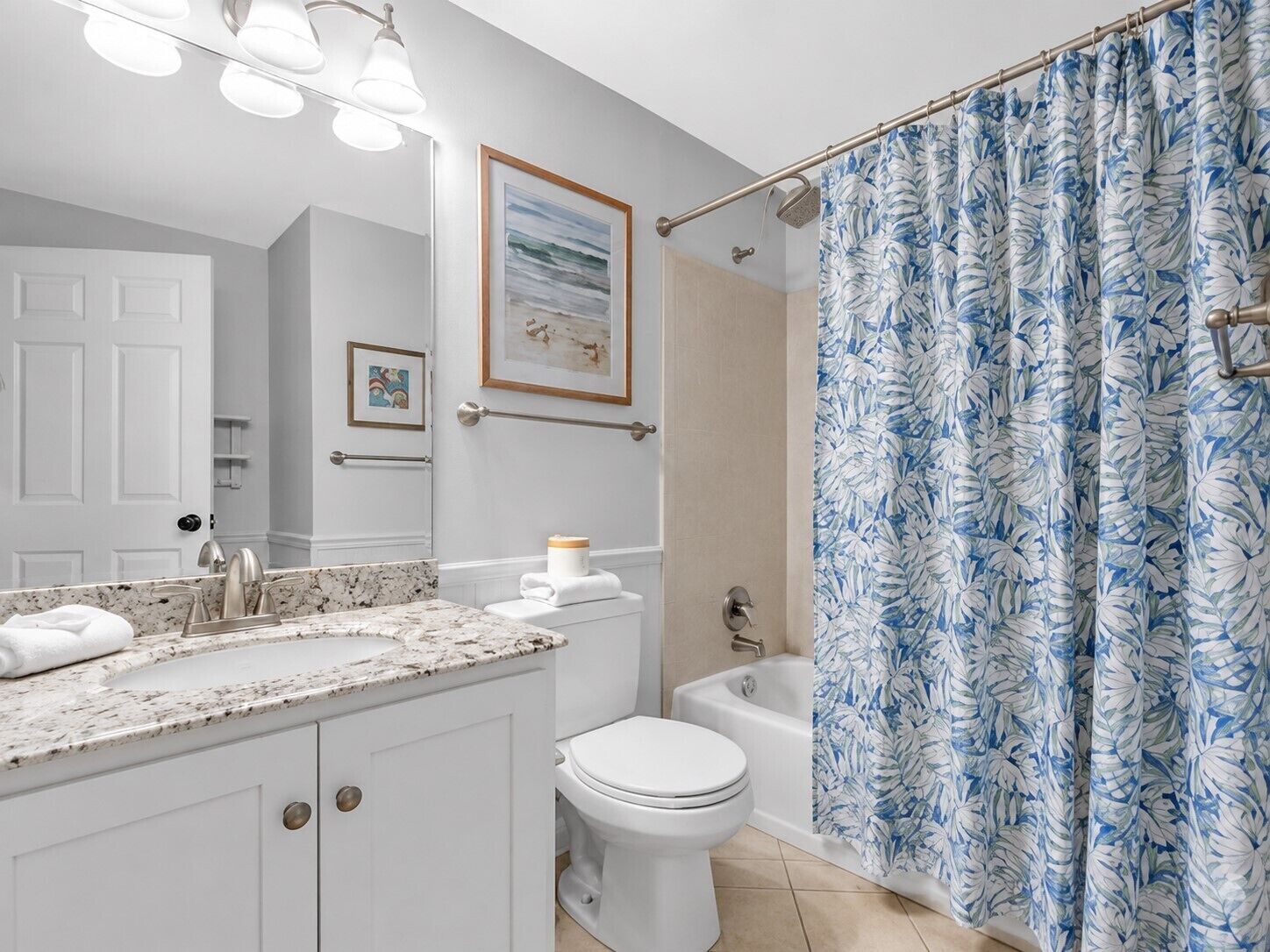 Une salle de bain avec un comptoir en marbre, des toilettes, une baignoire et un rideau de douche orné d’un motif de feuilles.