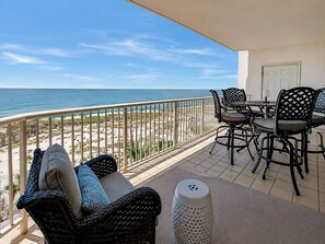 A balcony with a view of the beach and ocean, furnished with wicker chairs and a table.