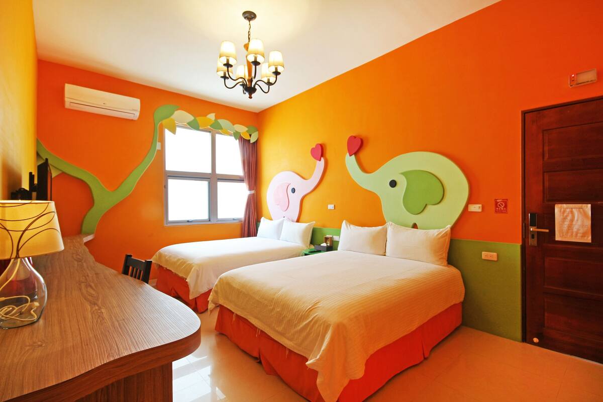 A hotel room with two beds, a chandelier, an air conditioner, and a window with curtains.