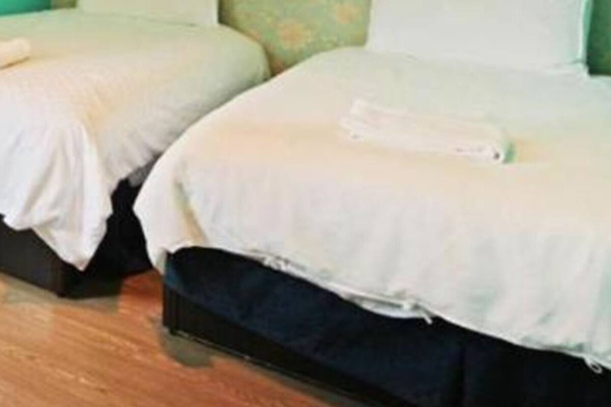 A room with two beds, a green floral wall, and a wooden floor.