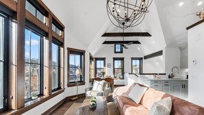 A spacious living room with large windows, a modern chandelier, and a cozy seating area. - Aurum Condo -1 BR w/ Mtn Views, Steps from Main St (Breckenridge)