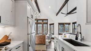 A modern kitchen with white cabinetry, a central island, and large windows providing natural light. - Aurum Condo -1 BR w/ Mtn Views, Steps from Main St (Breckenridge)