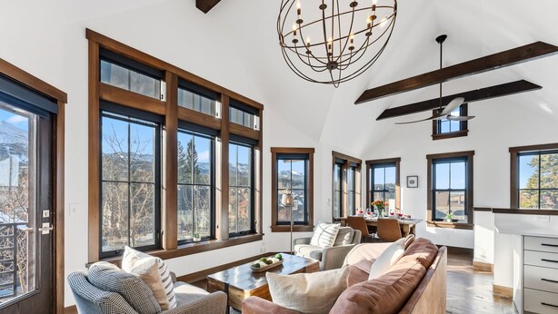 A spacious living room with large windows, a chandelier, and a modern kitchen in the background. - Aurum Condo -1 BR w/ Mtn Views, Steps from Main St (Breckenridge)