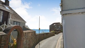 Calle estrecha con un arco de ladrillo, un edificio blanco y vista al mar con barcos.