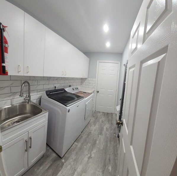 A compact kitchen with white cabinets, a stainless steel sink, a built-in oven, and a door leading to another room.