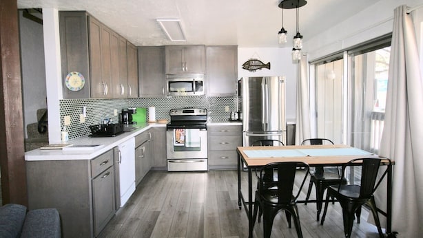 A modern kitchen with stainless steel appliances, a dining area with a wooden table and chairs, and large windows with curtains. - Spacious, upgraded Condo in Sierra Park Villas (Mammoth Lakes)
