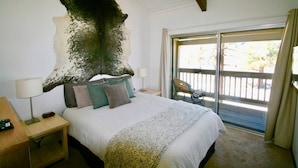 A bedroom with a large, textured wall piece, a bed with multiple pillows, a bedside table with a lamp, and a view of the outdoors through a sliding door. - Spacious, upgraded Condo in Sierra Park Villas (Mammoth Lakes)