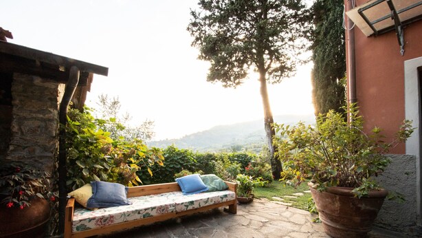 A stone patio with a wooden bench, potted plants, and a view of the countryside.
